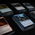A close-up, angled view of several Magic: The Gathering trading cards arranged on a dark surface. The central card is a blue Library Locus card, with other cards fanned out around it, showing various artwork and text.